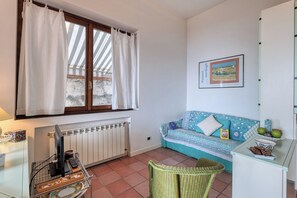 Una habitación acogedora con ventana, un radiador, un sofá, un sillón de mimbre y una mesita con un frutero.