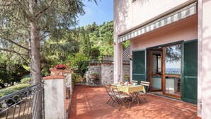 A terrace with a table and chairs, surrounded by greenery and a view of the sea. - Hanbury Apt Pool And Sea (Ventimiglia)