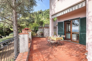 A terrace with a table and chairs, surrounded by greenery and a view of the sea. - Hanbury Apt Pool And Sea (Ventimiglia)