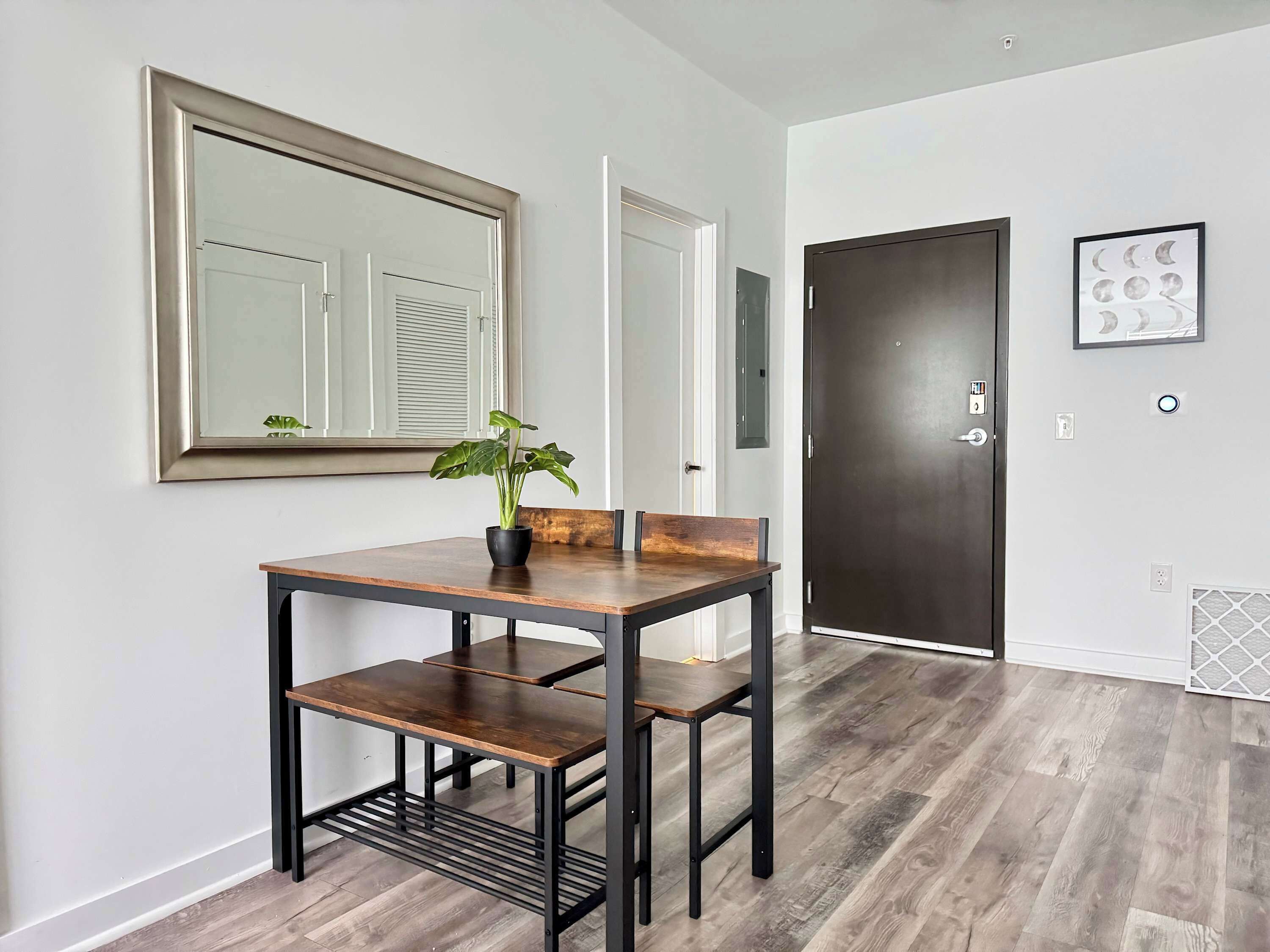Une pièce moderne avec une table et des chaises en bois, un grand miroir et une porte sombre.