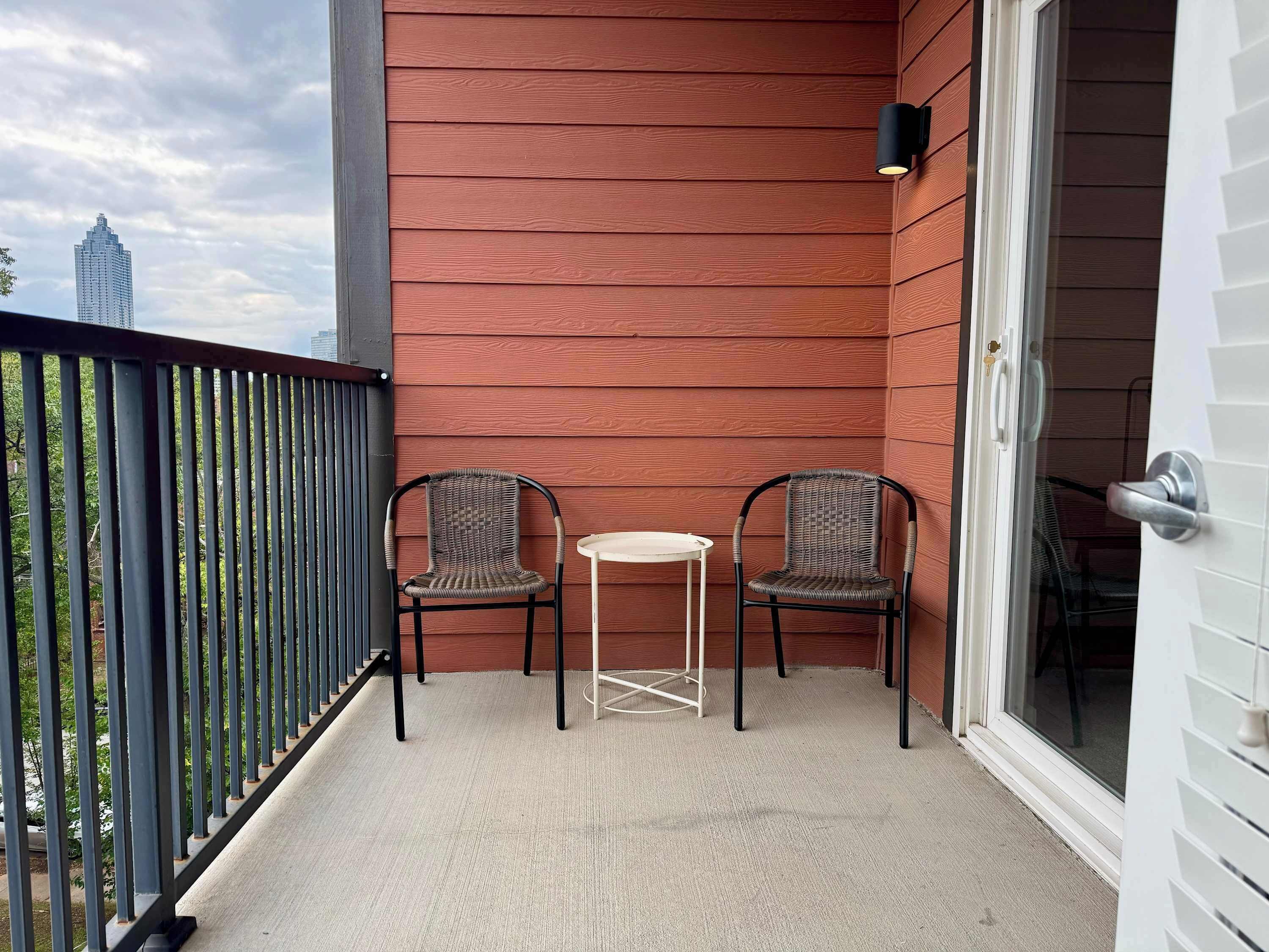 Ein Balkon mit zwei Korbstühlen, einem kleinen Tisch, einer roten Holzverkleidung und einem Metallgeländer.