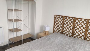 A bedroom with a bed, a wooden headboard, a white canopy, a nightstand with a lamp, and a wooden shelf unit. - APART 1 located 100 m from the beach (Bray-Dunes)