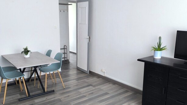 A modern kitchen with a dining area, featuring a wooden floor, a glass-top table, and a black cabinet with a cactus plant. - APART 1 located 100 m from the beach (Bray-Dunes)