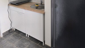 A compact kitchen with a black refrigerator, a sink, and a countertop with a laptop and a sponge. - APART 1 located 100 m from the beach (Bray-Dunes)