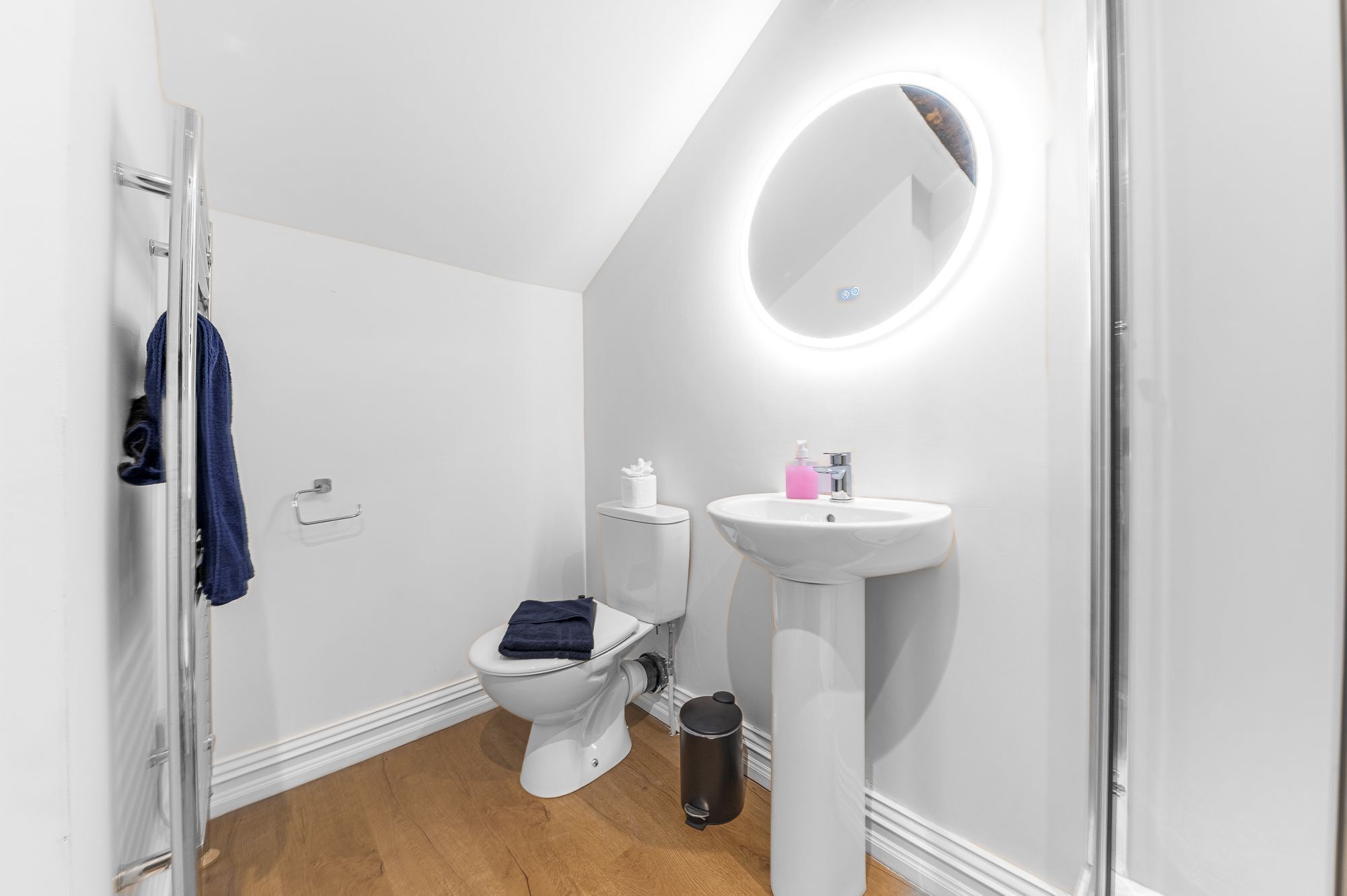 Un baño moderno con inodoro blanco, lavamanos pedestal y espejo.