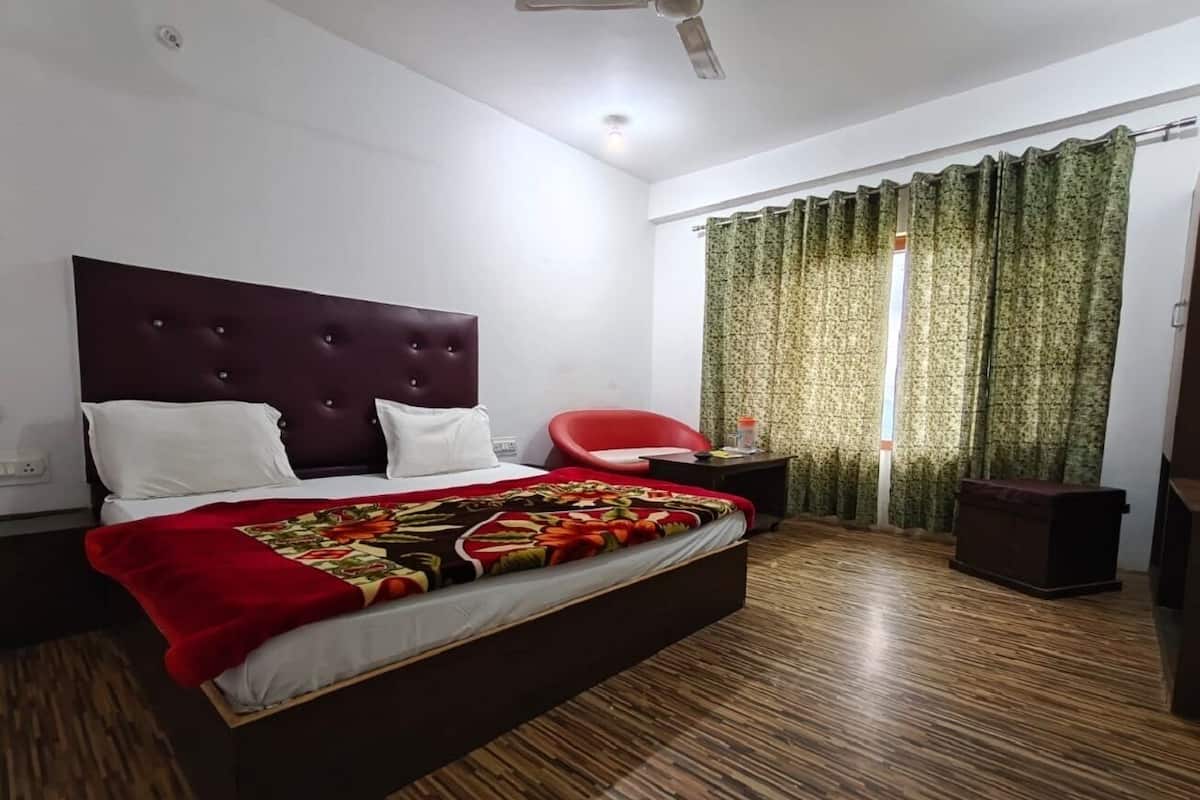 A bedroom with a bed, a red chair, a nightstand, and a window with curtains.