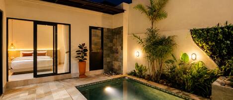 A modern outdoor pool area with a glass-enclosed bedroom, a stone shower, and ambient lighting.