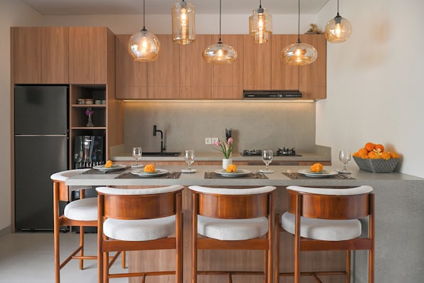 Una cucina moderna con mobili in legno, un'isola centrale con sgabelli da bar, illuminazione a sospensione e un'area da pranzo apparecchiata per quattro persone.