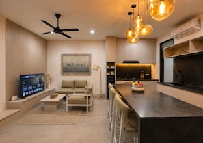 Una sala de estar moderna con televisor de pantalla plana, sofá, mesa de centro y un comedor con taburetes de bar.