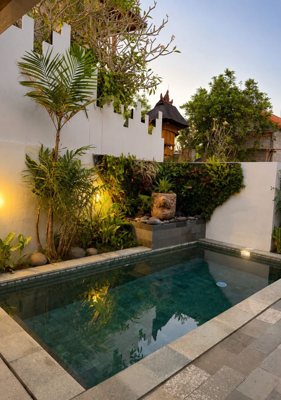 A swimming pool with a stone border, surrounded by lush greenery and a white wall.