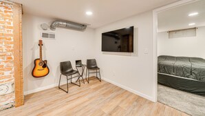 A small, modern room with a brick accent wall, a guitar, two chairs, a bed, and a mounted TV. - 2 Mi to Dtwn: Family Home in Cheyenne! (Cheyenne)