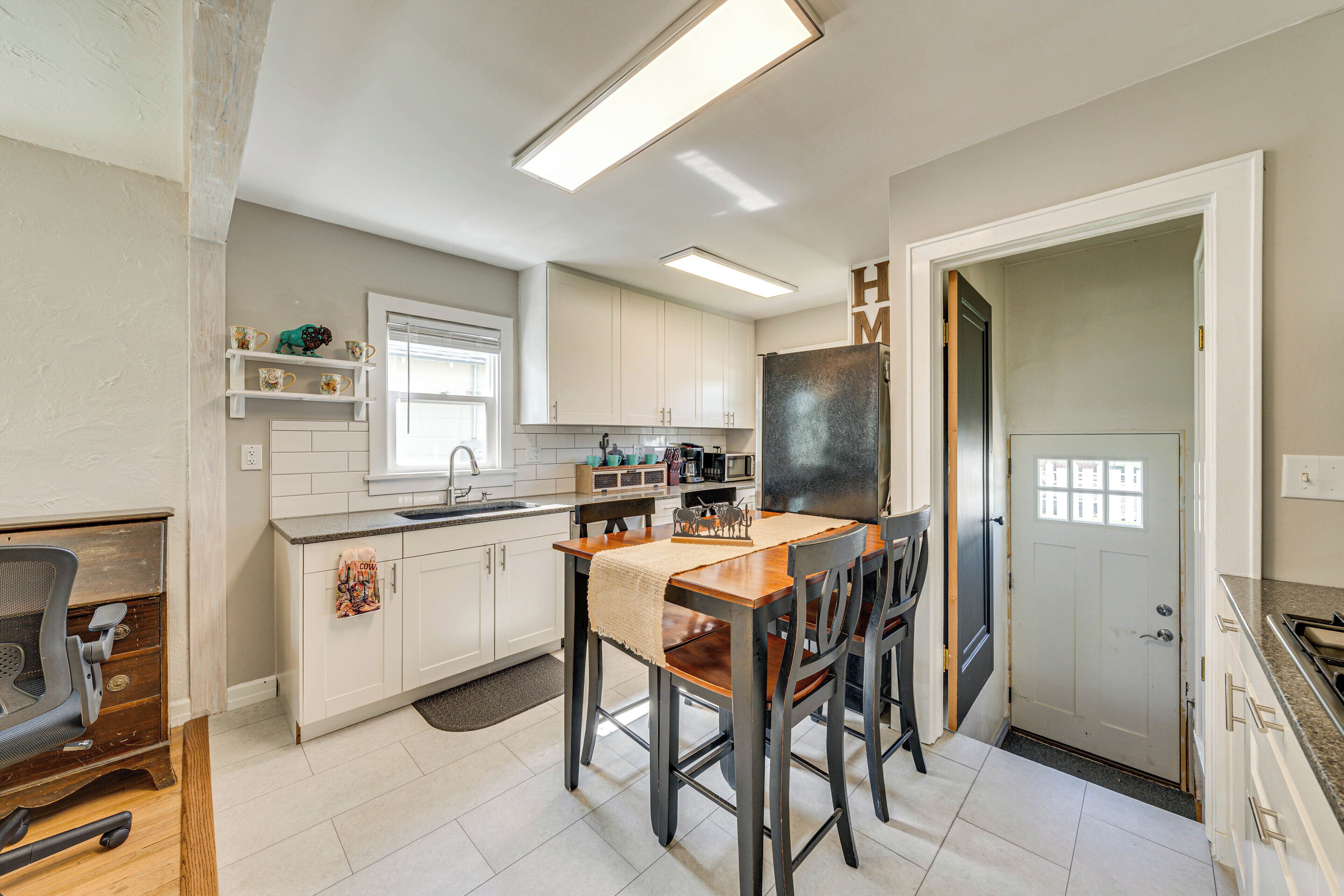 Una cocina moderna con armarios blancos, una mesa de comedor de madera y un refrigerador.