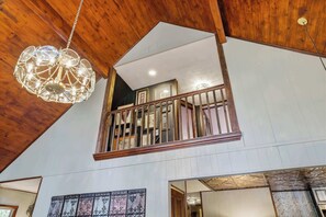 A multi-level interior with a wooden ceiling, a hanging light fixture, and a balcony with railings.