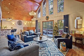 A spacious living room with a high ceiling, large windows, and a Christmas tree.