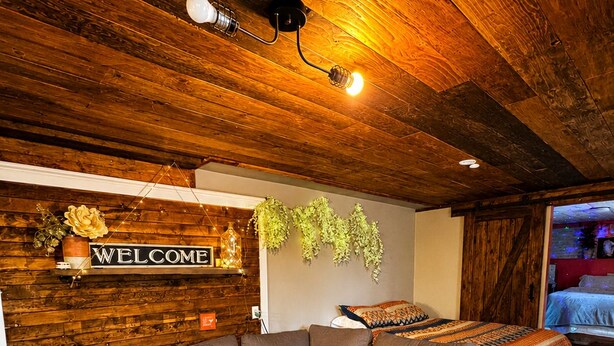 Una sala de estar moderna con un sofá seccional, un taburete de cuero, techo de madera y un letrero en la pared que dice 'WELCOME'.