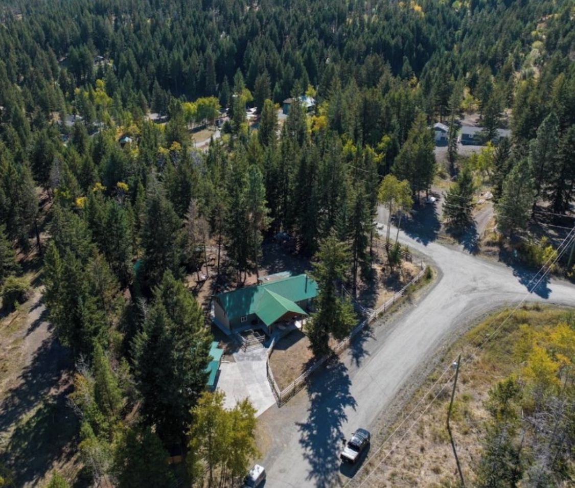 Une vue aérienne d’une propriété entourée d’une forêt dense, avec une allée sinueuse menant à un bâtiment doté d’un toit végétalisé.
