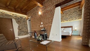 A modern room with a brick wall, wooden ceiling, a glass table, a sofa, and a bed. - EXORIA Luxury Rooms & Spa (Nuoro)