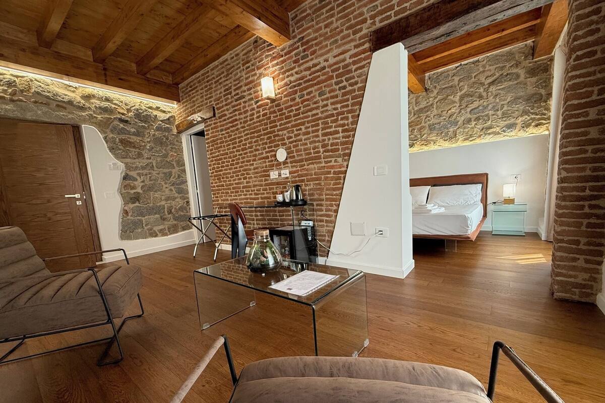 A modern room with a brick wall, wooden ceiling, a glass table, a sofa, and a bed.