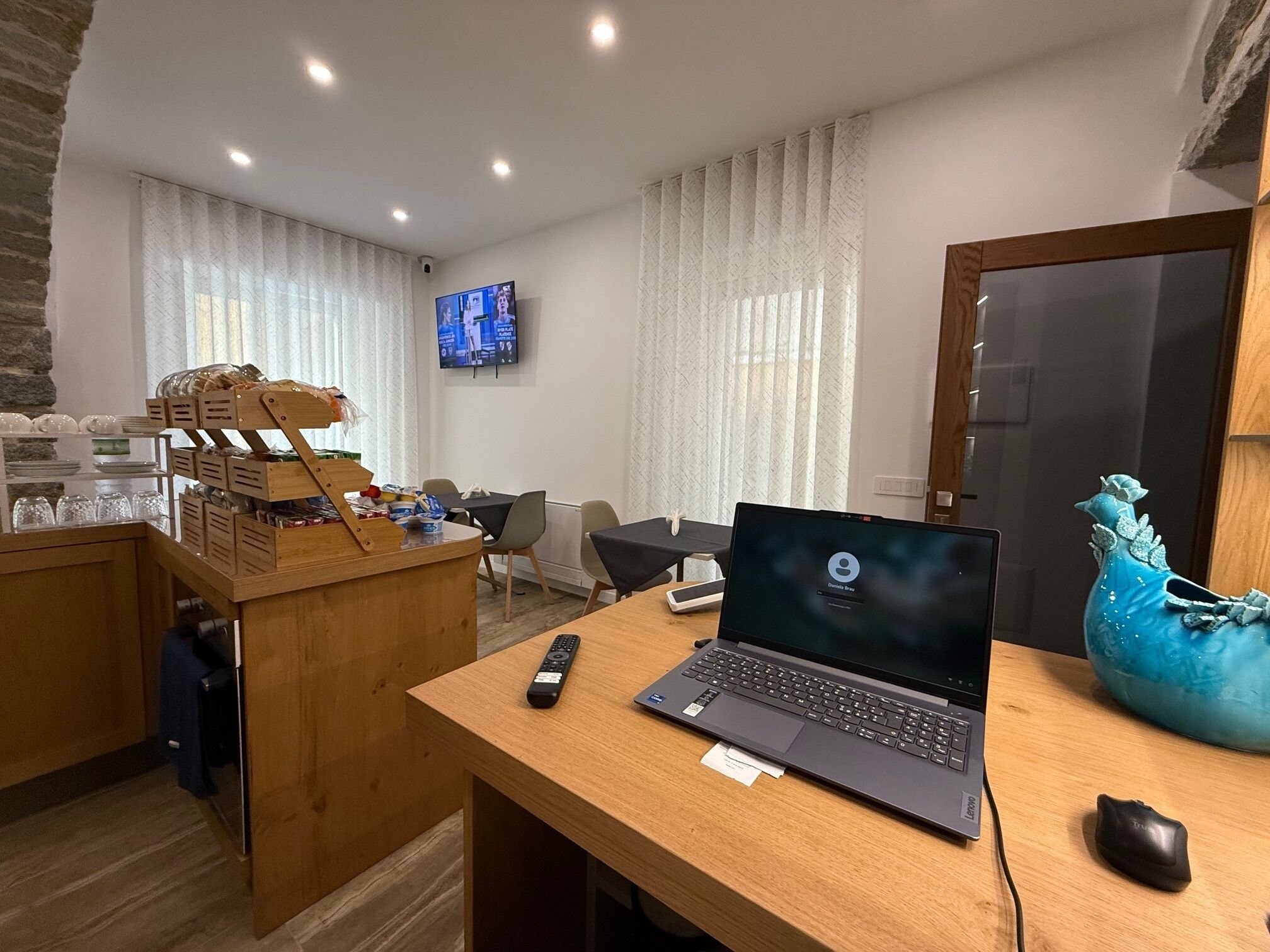 A hotel room with a wooden desk, a laptop, a remote control, and a decorative vase.