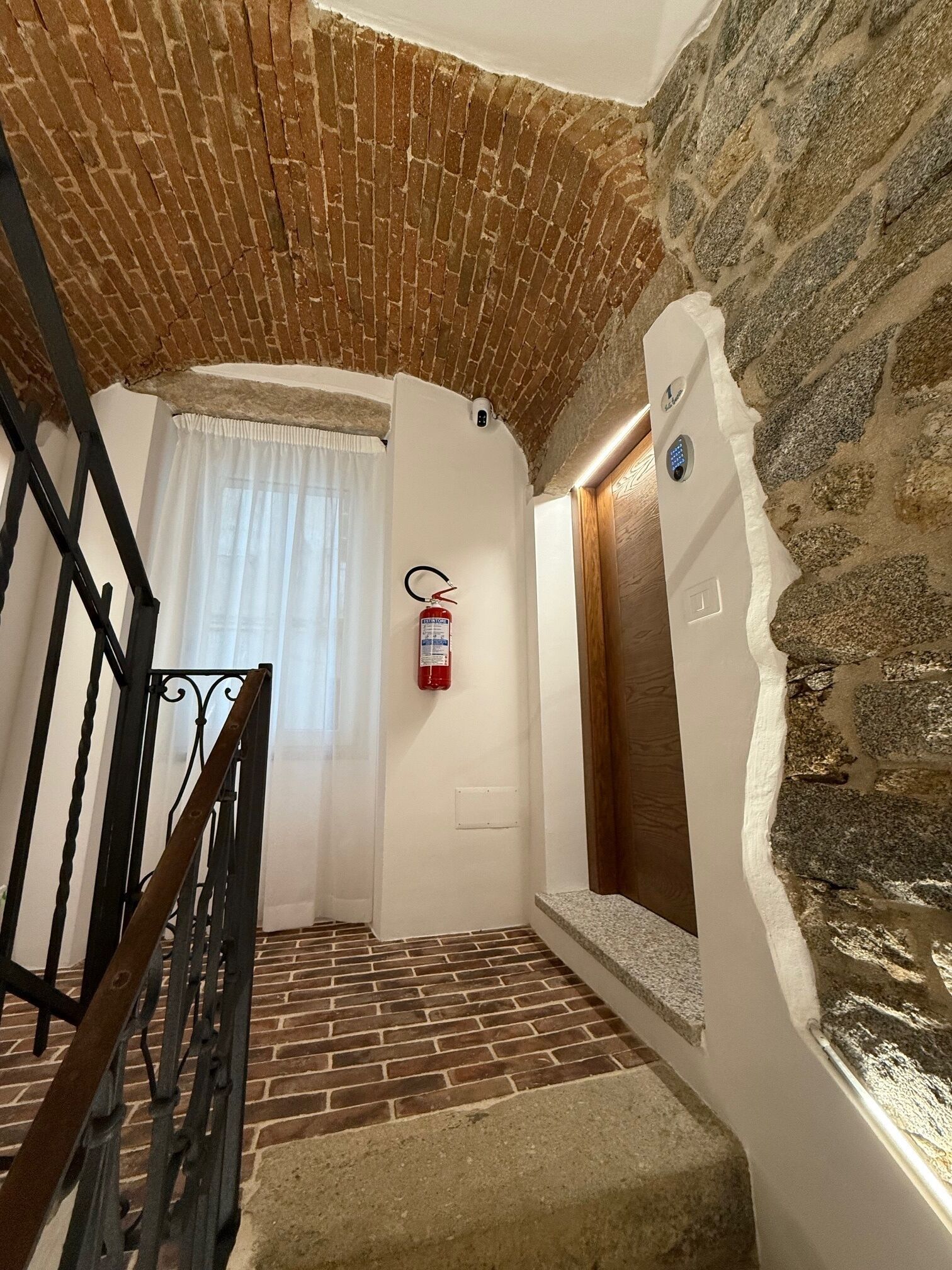 A staircase with a brick floor leading to a room with a stone wall and a wooden door.