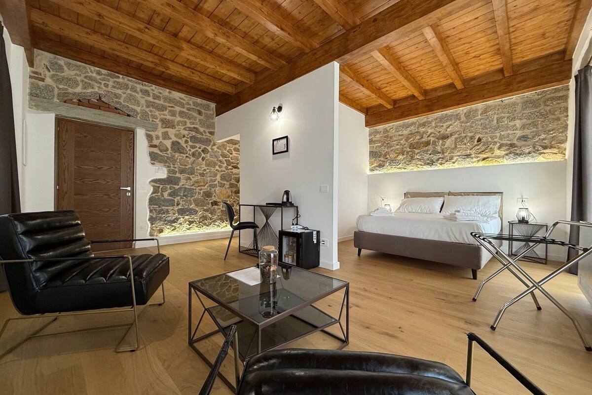 A modern room with a stone wall, wooden ceiling, a bed, a desk, and a chair.