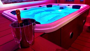 A hot tub with a bottle of champagne and two glasses on a wooden deck. - EXORIA Luxury Rooms & Spa (Nuoro)