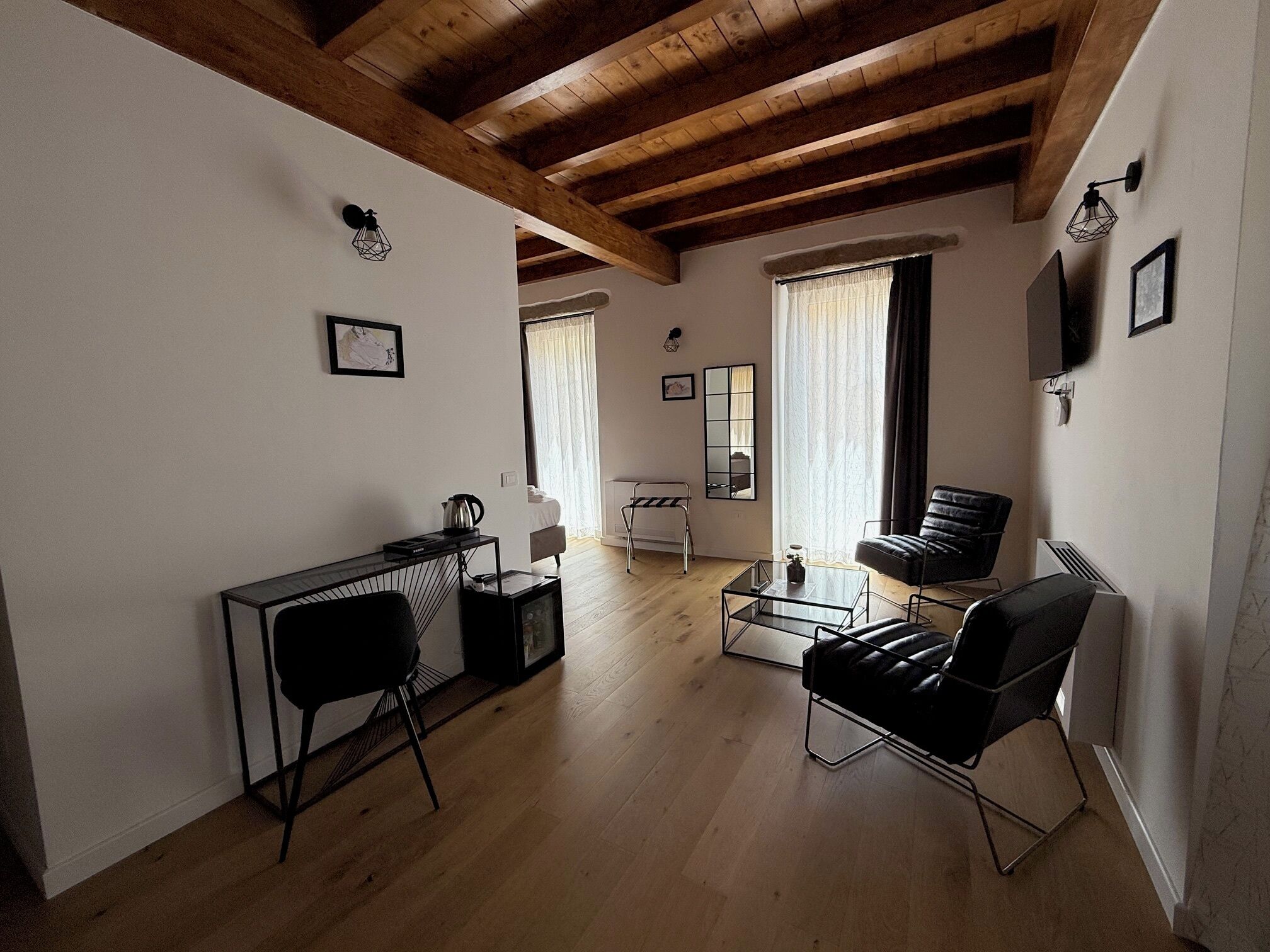 Una sala de estar moderna con techo de madera, un sofá de cuero negro, una mesa de centro de vidrio y una mesita auxiliar.