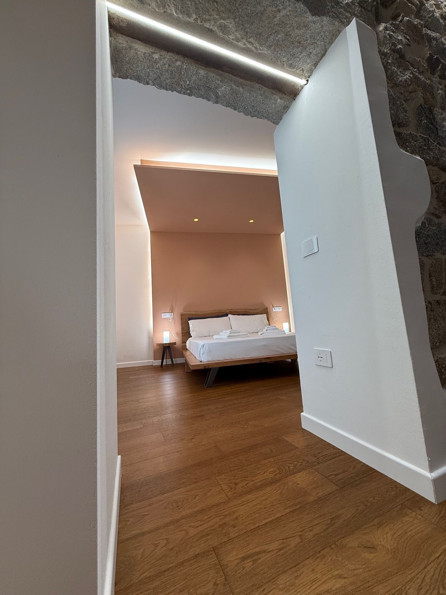 Una camera da letto moderna con pavimento in legno, un letto con lenzuola bianche e una parete in pietra.