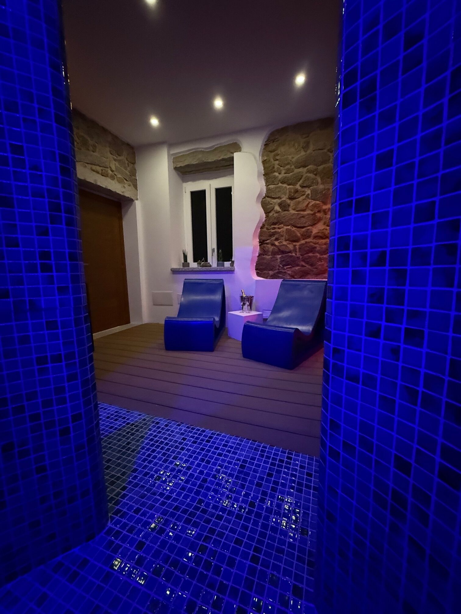 Un área de spa con dos sillas acolchadas en azul, una pared de piedra y un suelo de baldosas.