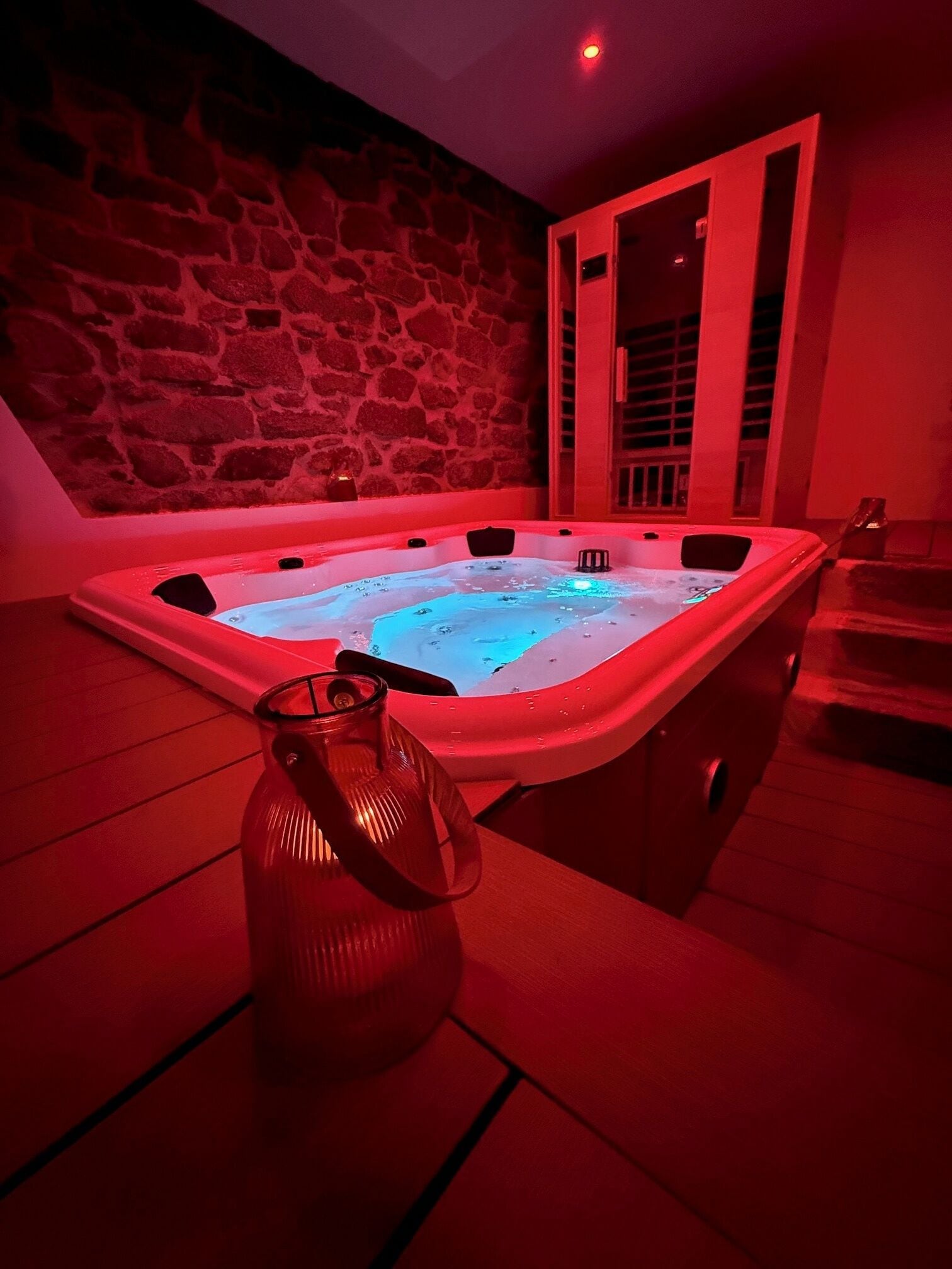 Un jacuzzi con un fondo de pared de piedra, un florero de vidrio y una iluminación roja.