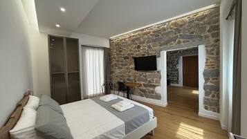 Un dormitorio con pared de piedra, una cama con almohadas, un televisor montado en la pared y suelo de madera.