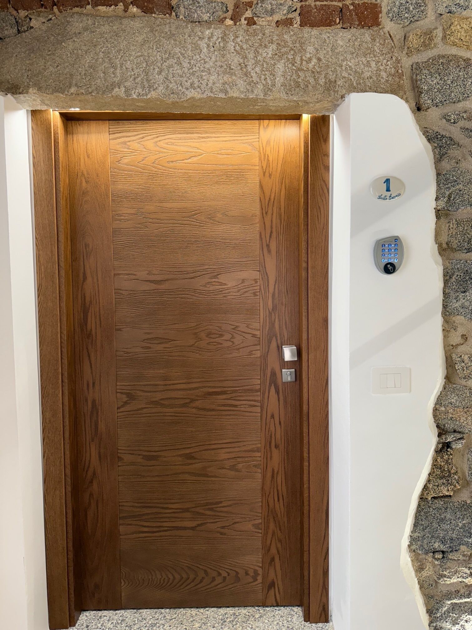 Una puerta de madera con un teclado numérico y un interruptor de luz en la pared a su lado.