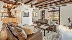 Amplia sala de estar con techo alto, vigas de madera, un sofá de cuero marrón, una mesa de centro y vistas al exterior.