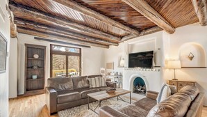 Una sala de estar acogedora con techo de madera, sofás de cuero, chimenea y televisor montado en la pared.