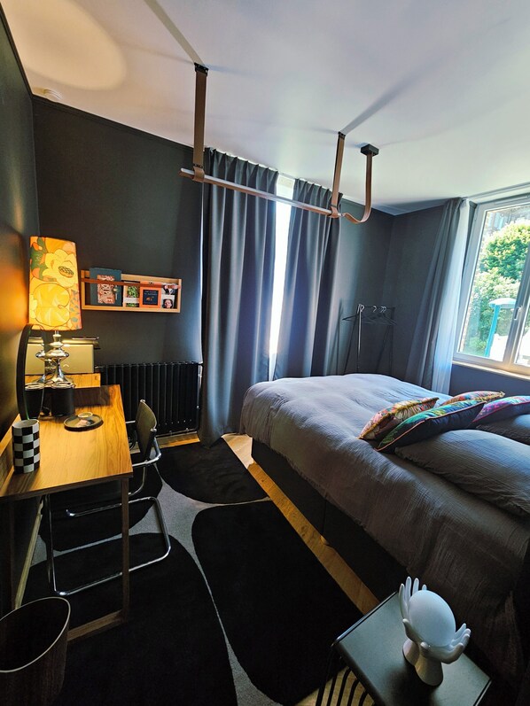 Une chambre d’hôtel moderne équipée d’un lit, d’un bureau, d’une lampe et d’une fenêtre avec des rideaux.