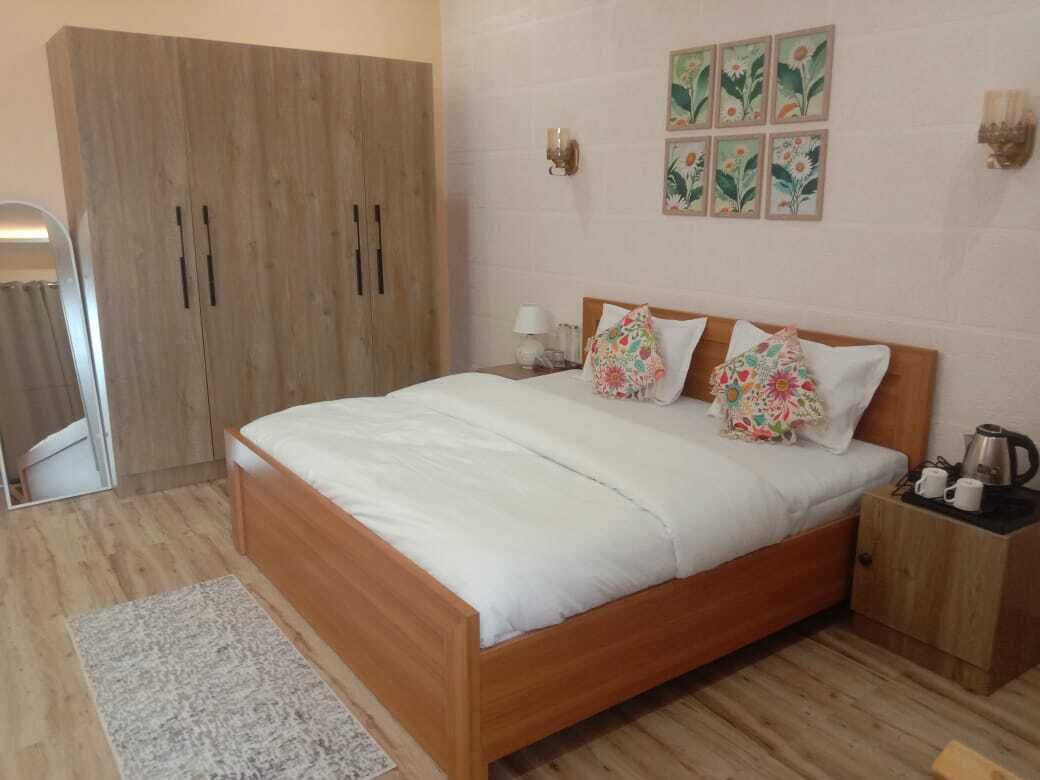 A bedroom with a wooden bed, a nightstand, a wardrobe, and a small table with a kettle.