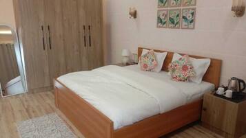 A bedroom with a wooden bed, a nightstand, a wardrobe, and a small table with a kettle.