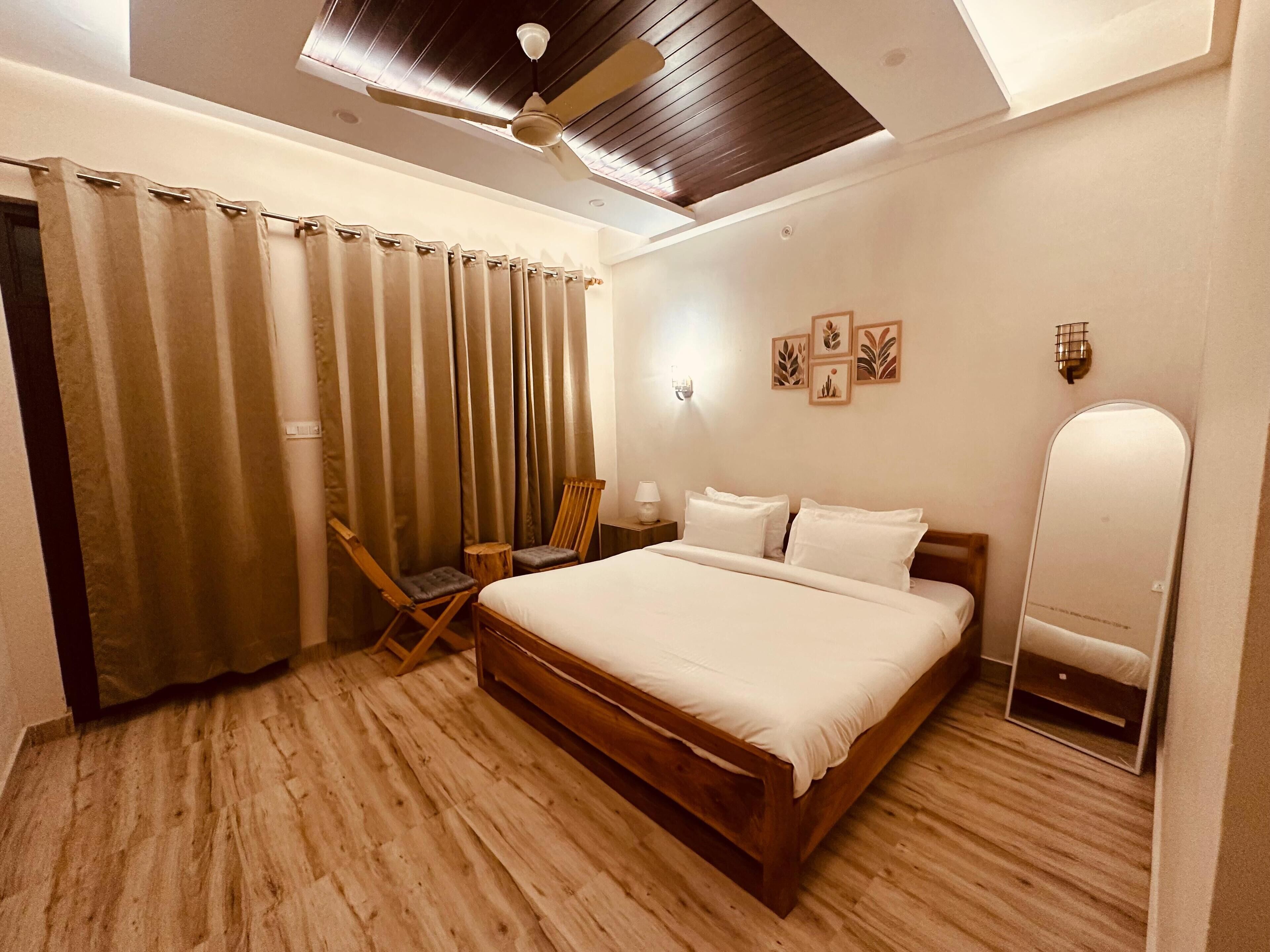 Une chambre à coucher avec un lit en bois, un ventilateur de plafond, un plancher en bois et une fenêtre avec des rideaux.