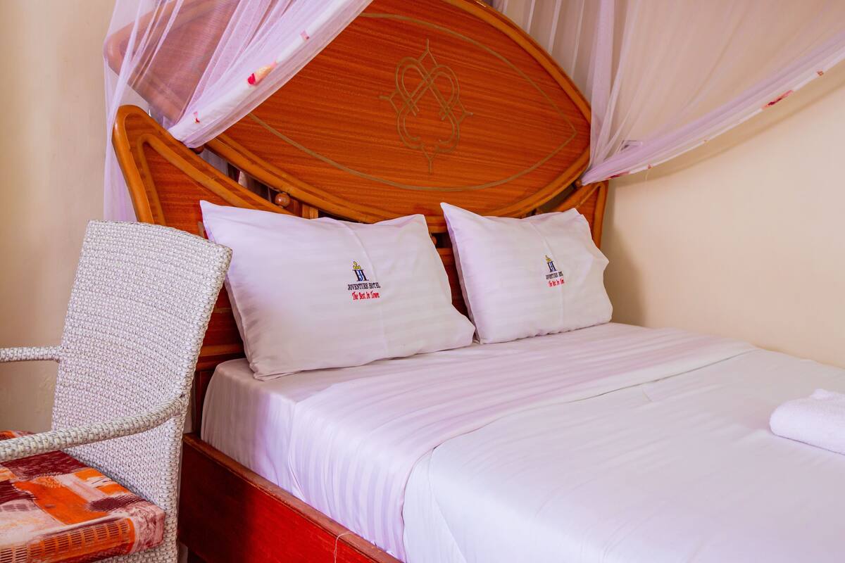 A bed with white bedding and pillows, a wooden headboard, and a white woven chair.