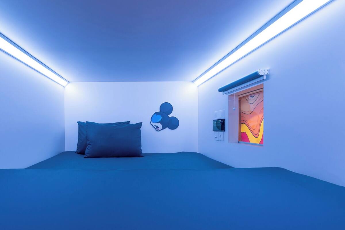 Una habitación con una cama, un adorno de Mickey Mouse montado en la pared y un cuadro abstracto de colores.