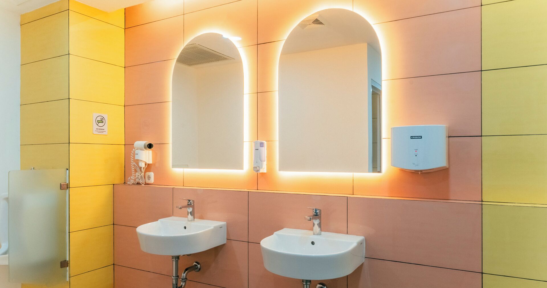A modern bathroom with two sinks, a mirror, and a hand dryer.
