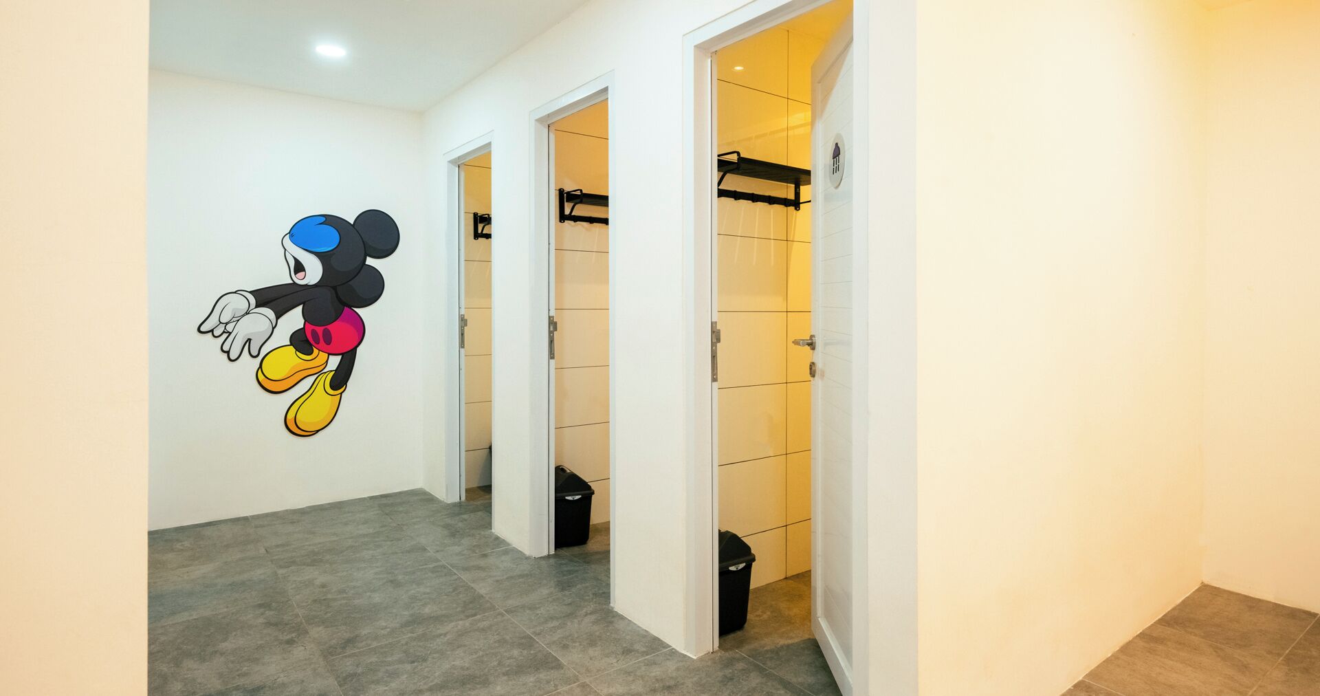 Un couloir décoré d’une fresque représentant Mickey Mouse, avec un sol carrelé gris et des murs blancs. On y trouve des portes donnant accès à une salle de bain et à un placard.