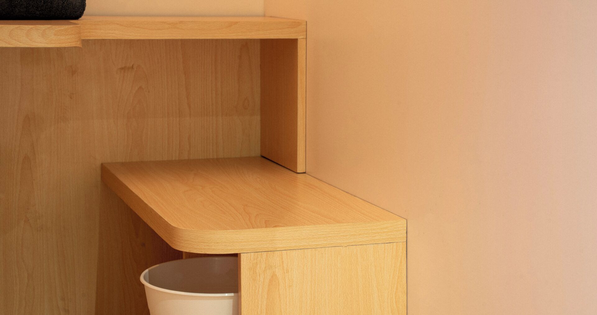 Un coin de pièce avec une étagère en bois et une poubelle blanche.