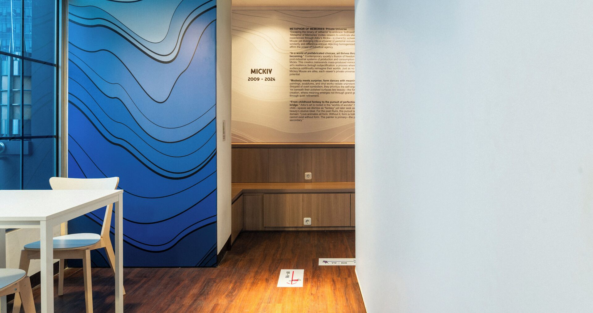 Un interior moderno con un muro azul abstracto, una mesa blanca y un banco de madera.