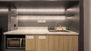 Una cocina moderna con encimera de mármol, horno empotrado y un lavabo con grifo. Hay señales que indican dónde se guardan los cubiertos, platos y tazas.