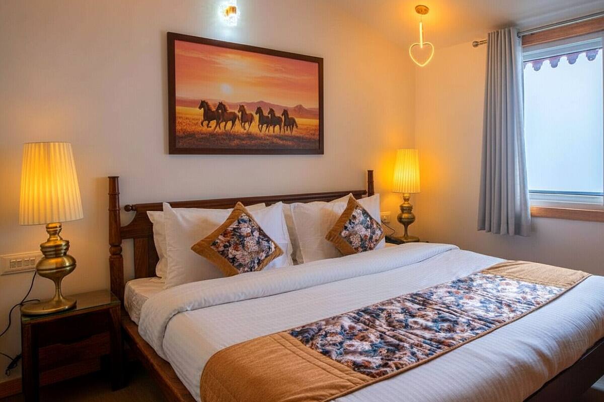 A neatly made bed with a floral-patterned bedspread, two bedside lamps, and a painting of horses on the wall.
