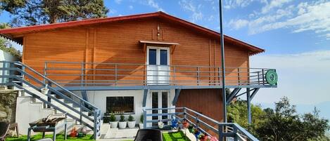 A wooden building with a red roof, a balcony, and a staircase leading to the entrance.