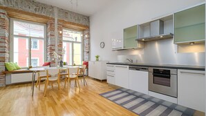 Une cuisine moderne avec des meubles blancs, des appareils en acier inoxydable et un coin fenêtre agrémenté de coussins.