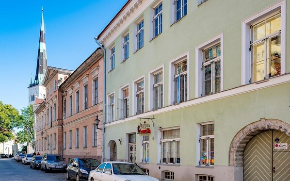 Une vue de rue avec des bâtiments historiques, le clocher d’une église et des voitures garées.