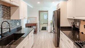 Una cocina moderna con muebles blancos, encimeras negras y un refrigerador de acero inoxidable.